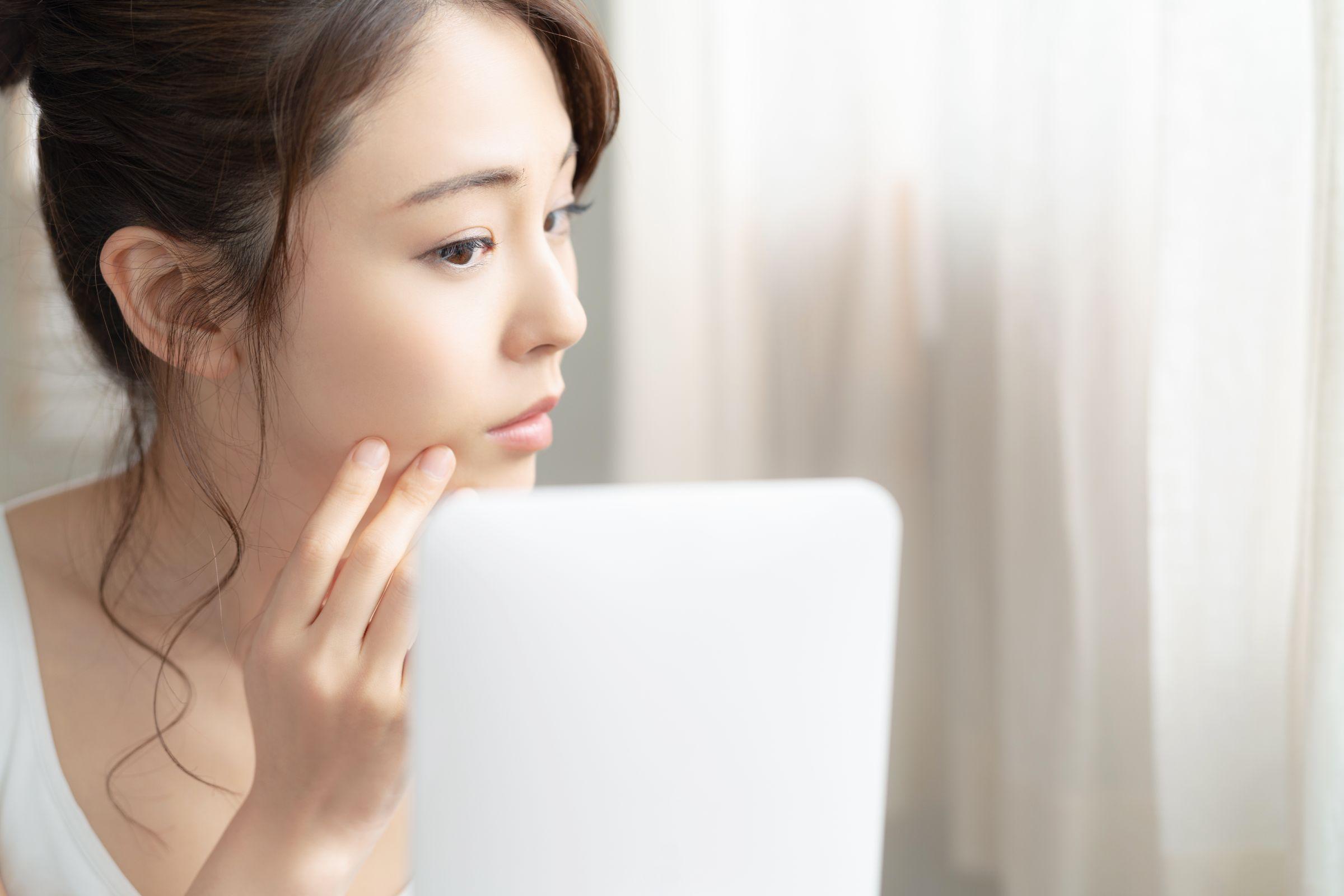 鏡で自分の頬を見て不安そうな女性